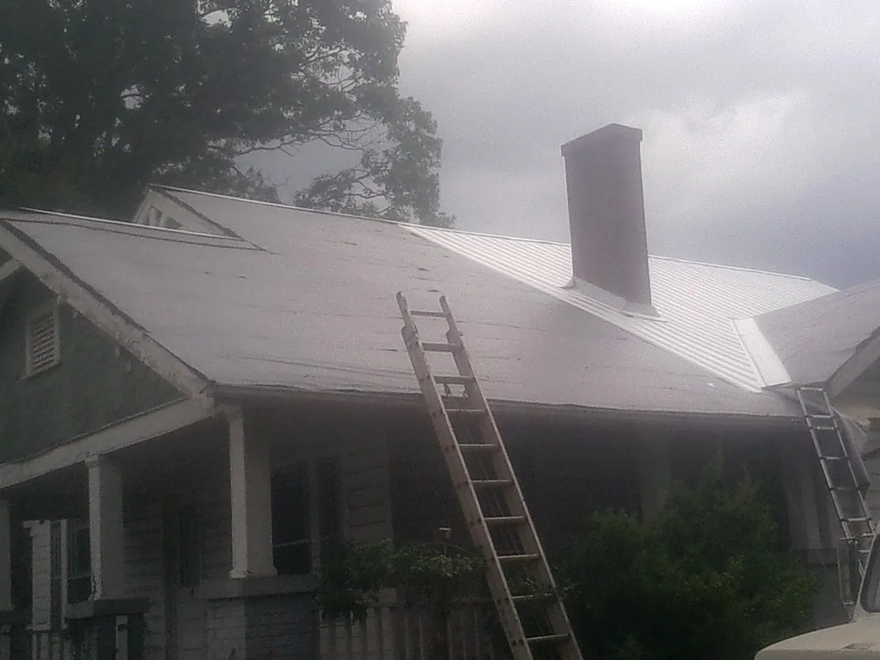 Ladders against a metal roof on an older home with a brick chimney in Pineville